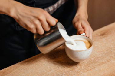 Baristaların elleri espresso bardağına sıcak süt döker. Cappuccino pişiriyorum..