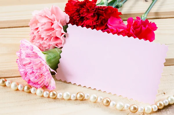 Hermosas flores de clavel en flor con papel de tarjeta rosa en blanco — Foto de Stock