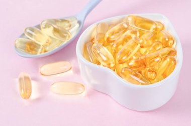 Pembe arka planda beyaz bardakta balık yağı kapsülleri.