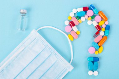 Aşı ve mavi arka planda cerrahi maskeli haplar..