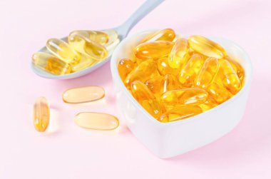 Pembe arka planda beyaz bardakta balık yağı kapsülleri.