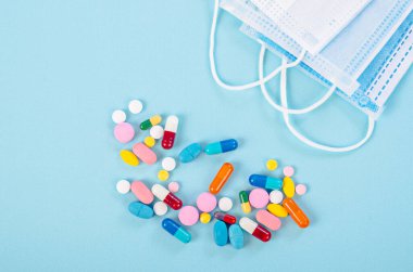 Mavi arka planda cerrahi yüz maskesi olan ilaç ve haplar..