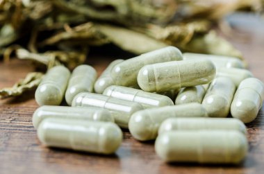 Kapsüllerde bitkisel ilaç yığını. Ahşap arka planda bitkisel yaprak..