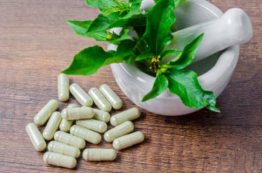 Kapsüllerde bitkisel ilaç yığını ve ahşap arka planda yeşil yapraklı seramik havan..