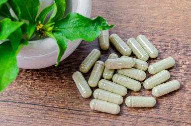 Kapsüllerde bitkisel ilaç yığını ve ahşap arka planda yeşil yapraklı seramik havan..