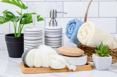 Duş süngeri, bitkisel sabun ve şampuan şişesi parlak bir banyo arka planında..