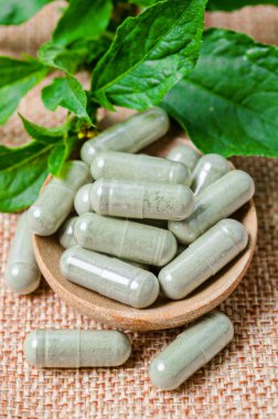 Pile of herbal medicine capsules in wooden spoon with green leaf on sack background. clipart