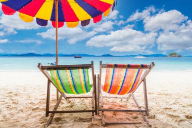 Sahilde şemsiyeli iki renkli plaj sandalyesi.