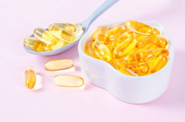 Pembe arka planda balık yağı kapsülleri olan kalp şeklinde bir tabak.