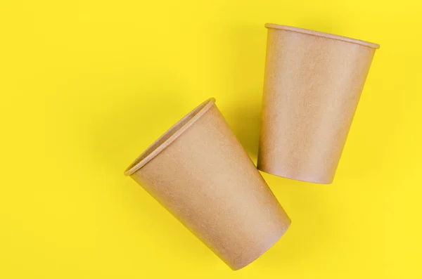 Disposable Brown paper cup for coffee, tea, a drink from environmental materials on a yellow background.