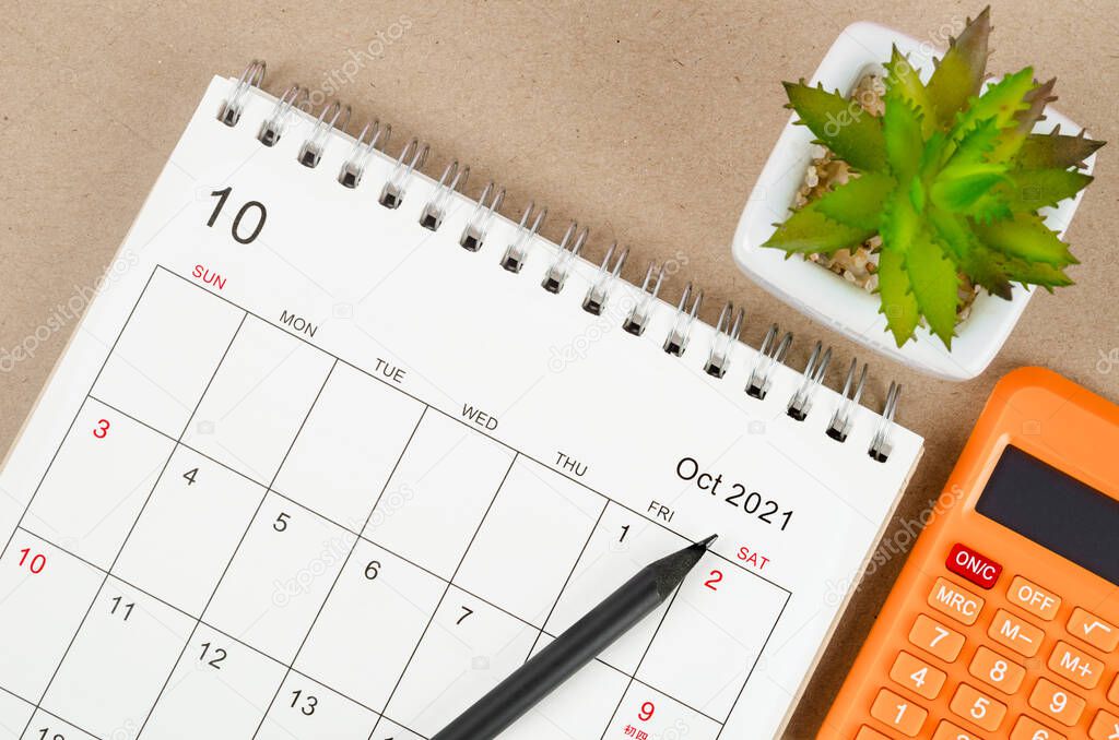 October 2021 desk calendar with calculator on wooden table.