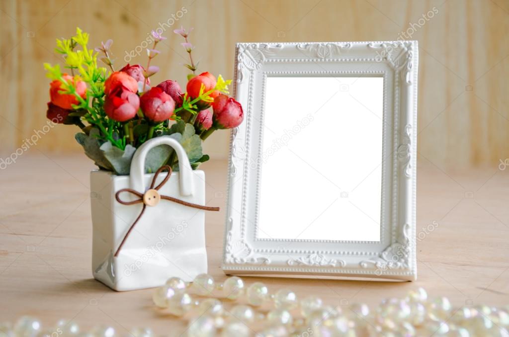 Flowers vase and blank white picture frame on wooden