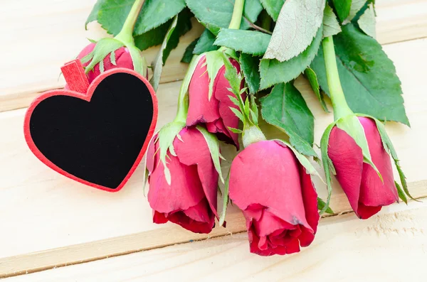 Etiqueta de madera en blanco forma de corazón con rosas rojas . — Foto de Stock