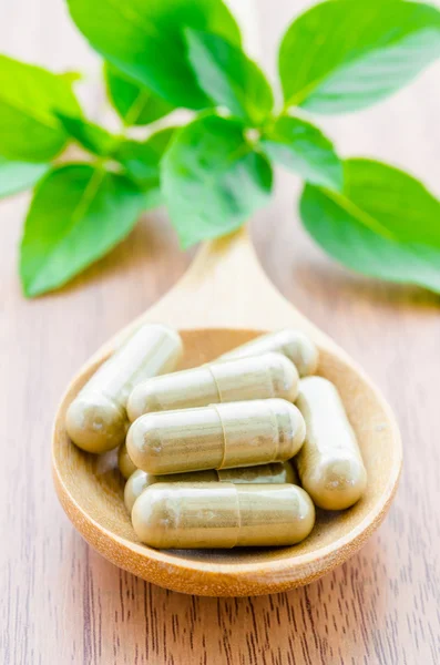 Cápsulas de hierbas medicinales en cuchara de madera . — Foto de Stock