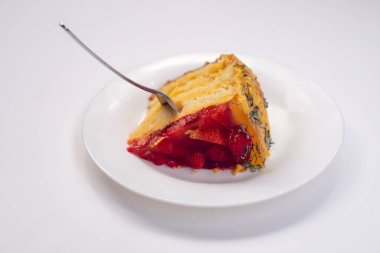 Beyaz bir tabakta lezzetli, tatlı bir meyveli pasta. Yanında metal bir kaşık var..