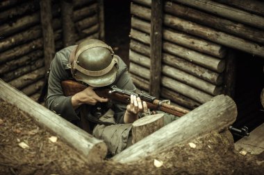 İkinci Dünya Savaşı 'nın askeri keskin nişancısı, ormandaki bir kulübede. Çelik bir miğferin başındaki tüfeğin ellerinde.