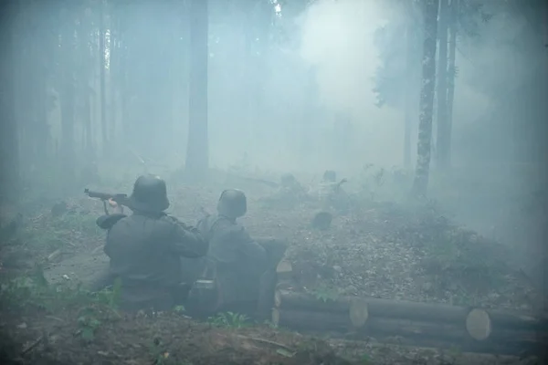 Soldiers in helmets with guns in their hands repel the enemy\'s attack. Big fog in the pine forest.