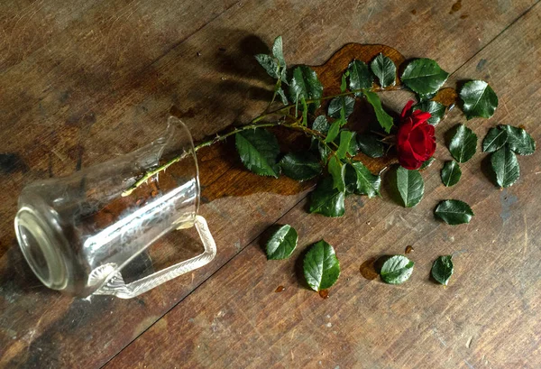 A broken glass vase with a red rose in it. broken love