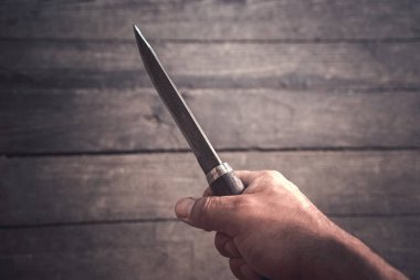 Karanlık bir arka planda büyük bir bıçakla bir adamın eli.