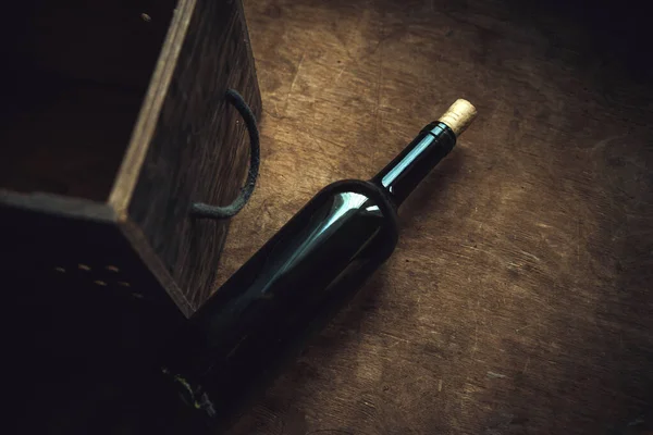 A dark bottle of wine with a gray stopper next to a wooden box on a vintage table in a retro style.