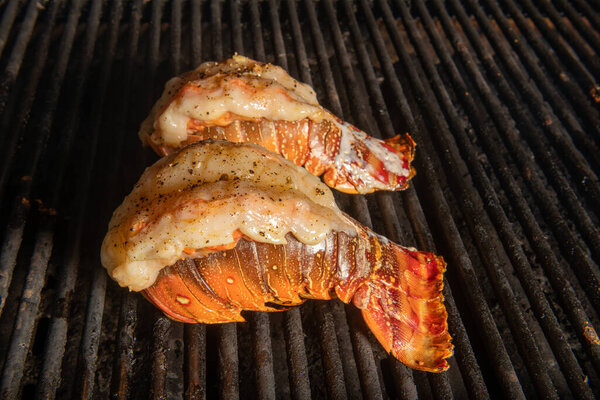 Lobster tails being cooked on a grill that is saddleback or buttflied