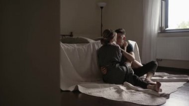 Genç ve güzel bir çift romantik vakit geçiriyor. Yatağın yanında oturmuş, sarılıyor ve gülümsüyor.