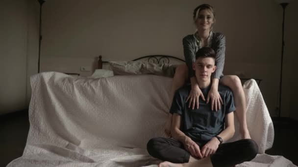Jovem lindo casal lindo sentado ao lado da cama e olhando para a câmera — Vídeo de Stock