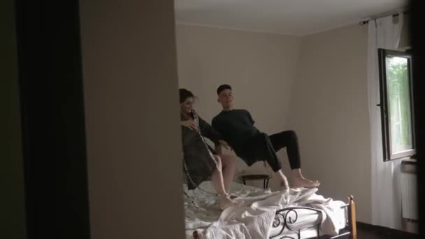 Funny man and woman falling on the bed and looking at each other and kissing. Young couple lying in the bed. Tender romantic relationship. Restful time together. Slow motion — Stock Video