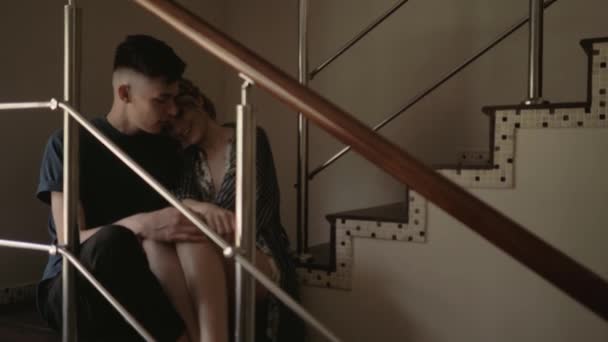 Młoda szczęśliwa i kochająca się para rozmawia i uśmiecha się siedząc na schodach w salonie swojego domu — Wideo stockowe