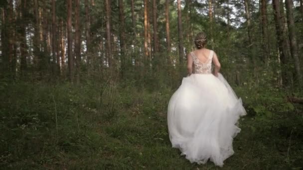 Krásná mladá veselá a radostná nevěsta ve svatebních šatech běží a točí se v lese. Utekla od kamery a otočila se. Zpomalený pohyb — Stock video