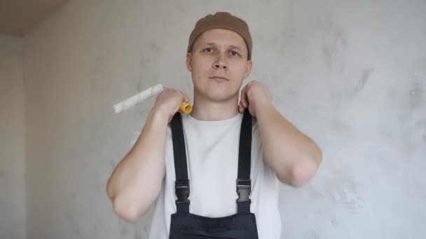 Een man in de bouw overalls toont gelukkig een verfroller aan de camera — Stockvideo