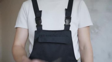 Tulumlu bir erkek inşaat işçisi kameraya düz bir tornavida gösteriyor.. 