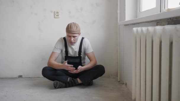 Un uomo sta riposando vicino al muro dopo il lavoro fatto per riparare l'appartamento. — Video Stock