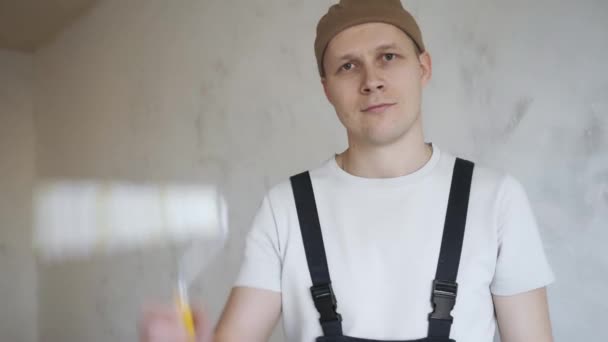 En man i bygg overaller visar gladeligen en färg roller till kameran — Stockvideo
