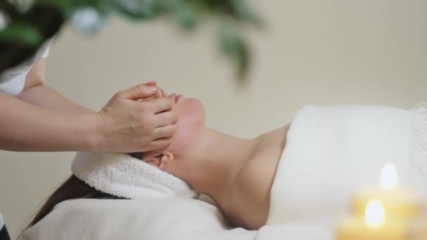 Söt brunett kvinna på ansiktsmassage i spa salong. Wellness ansikte massage spa — Stockvideo