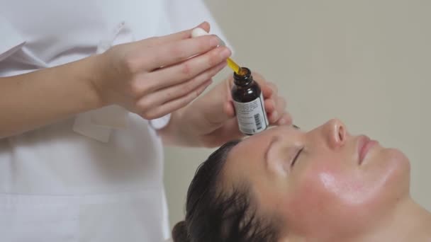 Aplicando aceite de masaje en la frente de una hermosa morena en el salón de spa — Vídeos de Stock