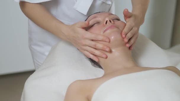 Linda mujer morena en masaje facial en el salón de spa. Wellness masaje facial spa — Vídeo de stock