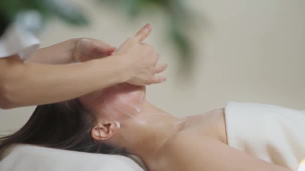Söt brunett kvinna på ansiktsmassage i spa salong. Wellness ansikte massage spa — Stockvideo