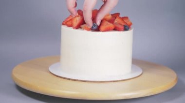 Genç bir kadının elleri, beyaz bir pastayı ahşap bir tepside meyvelerle süslüyor..