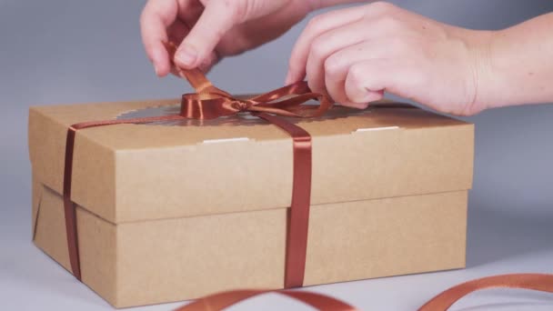 Manos de una mujer joven empaquetan cupcakes en una caja de artesanía con un lazo de cinta. — Vídeos de Stock
