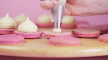 Pembe arka planda açık kremayla doldurulmuş güzel pembe badem kurabiyeleri.