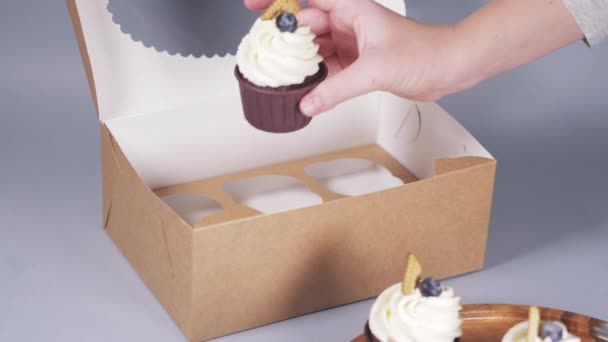 Руки молодой женщины пакуют кексы в коробку с лентой. — стоковое видео