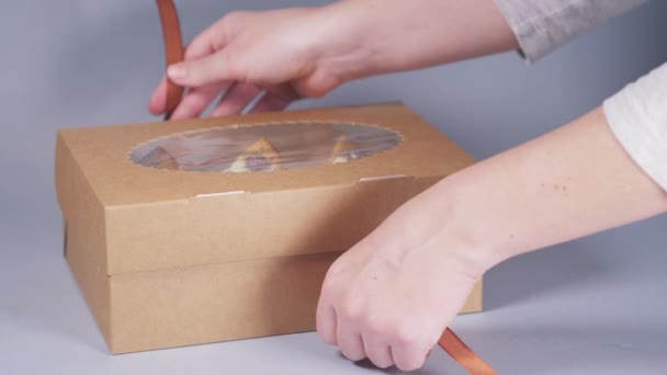 Ręce młodej kobiety pakują babeczki do pudełka ze wstążką.. — Wideo stockowe