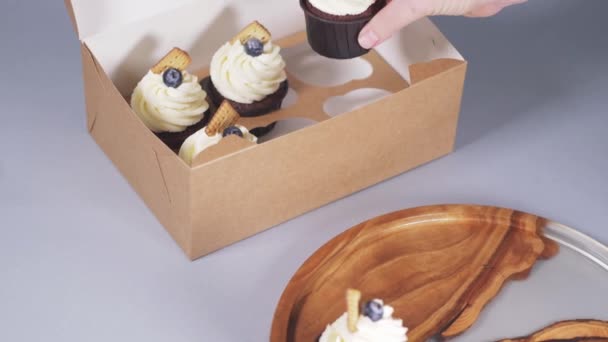 Ruce mladé ženy balení cupcakes v řemeslné krabici s mašlí luk. — Stock video