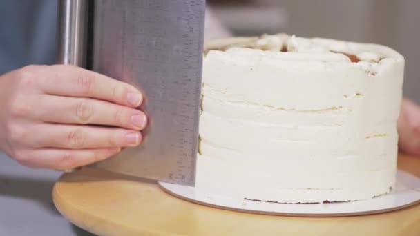 Vrouw nivelleren een lichte crème op een taart op een roterende stand in een huis keuken — Stockvideo