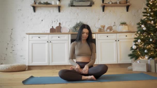 Une jeune femme est assise dans une position Lotus à la maison avec une décoration de Noël. — Video