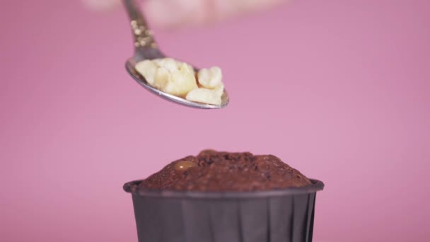 Primer plano sobre un fondo de rosa en una magdalena de chocolate con una cuchara, poner las nueces — Vídeo de stock