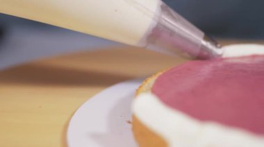 Pasta şefi kremayı bisküviler arasındaki böğürtlen katmanına sürüyor..