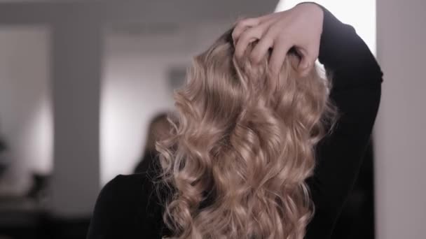 Loira endireita o cabelo com a mão, mostrando o estilo dos cachos ondulados — Vídeo de Stock