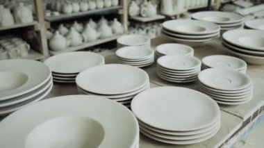 Üretim atölyesinin raflarında beyaz seramik tabaklar var.